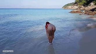 Naked red-haired girl bathes on a public beach